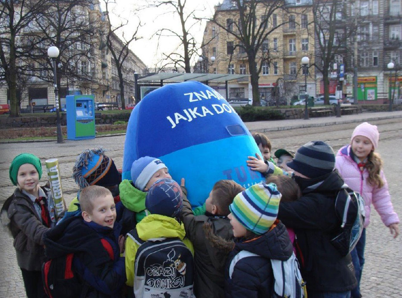 Na fotografii widnieje kostium reklamowy w postaci jajka pozujący do zdjęcia w towarzystwie dzieci w Szczecinie